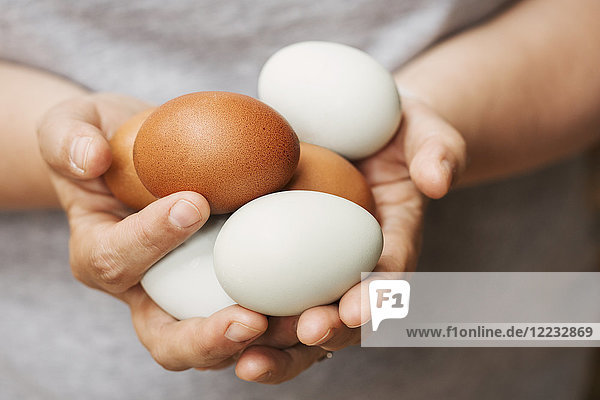 Eine Frau hält Hände voller frischer brauner und weißer Eier.