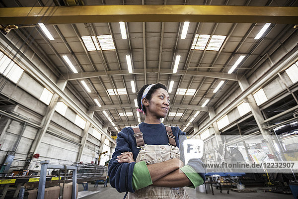 Black woman factory worker wearing coveralls in a large sheet metal factory.
