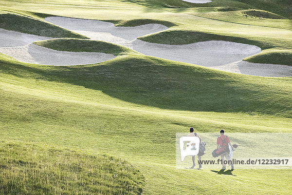 View from above of two golfers walking on a fairway toward the green of a golf course.