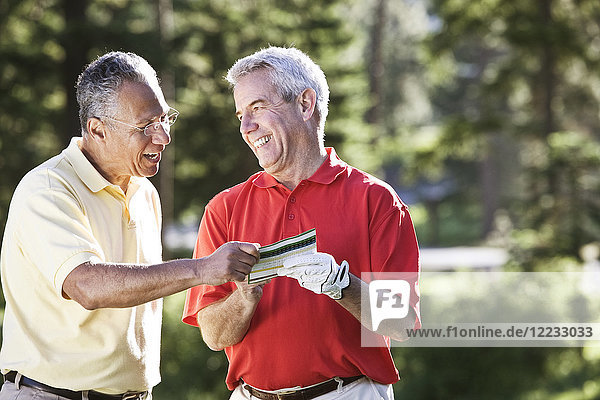 Zwei ältere Freunde lachen über einen Golfscore auf einem örtlichen Golfplatz.