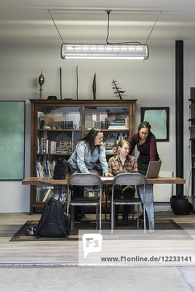 Three women gathered around table in office area of a metal workshop.