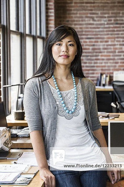 Asiatische Frau an ihrem kreativen Büroarbeitsplatz.