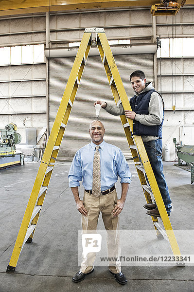 Black man factory owner and young Caucasian man factory worker goofing off together on the floor of a sheet metal factory.