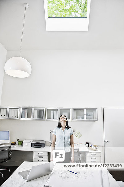 Hispanic woman looking up at a skylight in an architect's office.