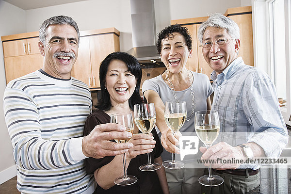 Two couples in a kitchen  Asian and Caucasian men and women making a toast with glasses of white wine.