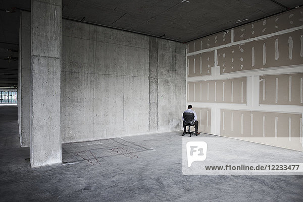 Business person sitting in the corner of a large empty raw office space.