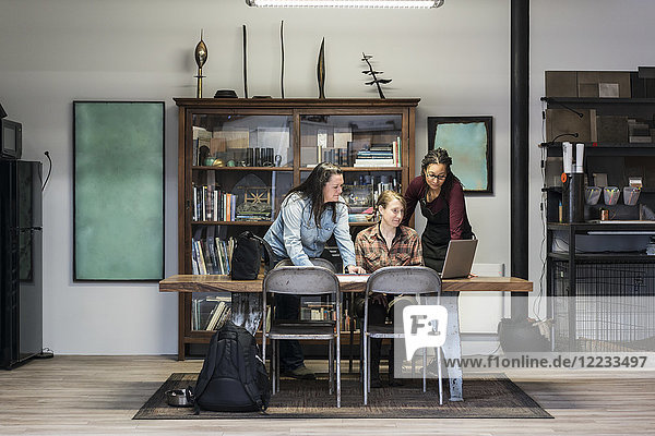 Three women gathered around table in office area of a metal workshop.