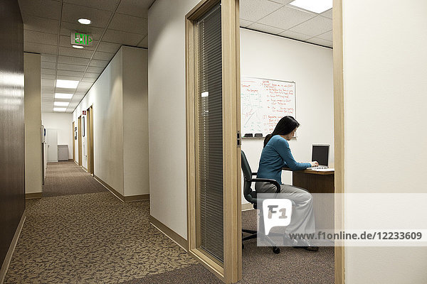 View down a hallway with an Asian woman in a meeting in an office.