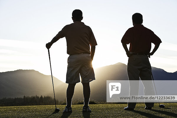 Zwei ältere Freunde nähern sich bei Sonnenaufgang dem ersten Abschlag eines Golfplatzes.