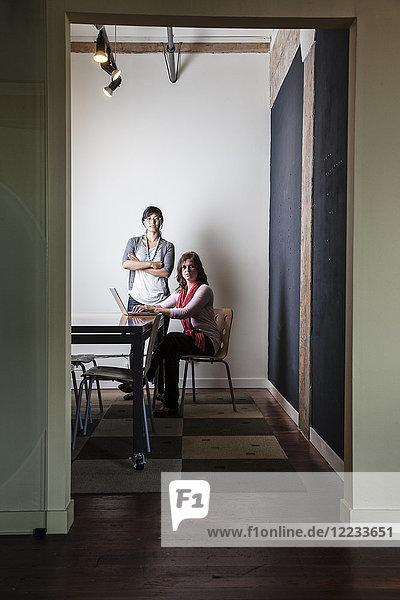 Caucasian woman and Asian woman working on a laptop computer in a small conference room.
