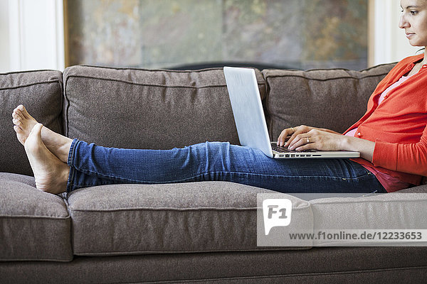 Mixed race Caucasian woman at home on the couch working on a lap top computer with her feet up.