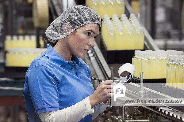Eine kaukasische Angestellte  die ein Kopfnetz trägt und an einer Produktionslinie in einer Abfüllanlage arbeitet.