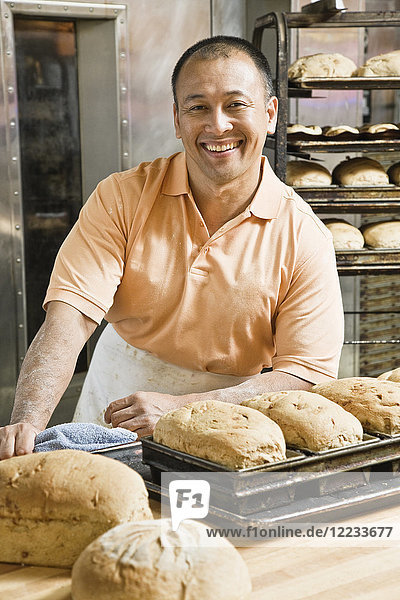 Hispanic man baker and some of the loaves of bread he baked this morning.