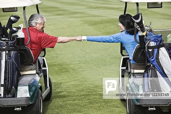 Ein älteres Paar  das auf dem Fairway eines Golfplatzes einen Fausthieb zwischen Golfwagen ausführt.