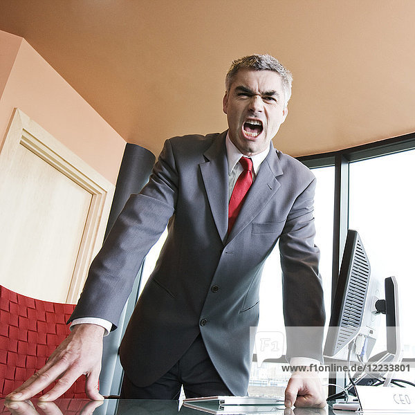 An angry Caucasian businessman in a suit and tie yelling at the viewer of the photograph.