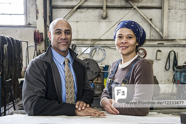 Schwarzer Besitzer einer Blechfabrik und eine schwarze Fabrikarbeiterin besprechen Pläne an einem Arbeitsplatz auf dem Boden der Fabrik.