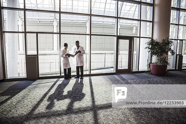Man and woman doctors conferring over medical records in a hospital lobby.