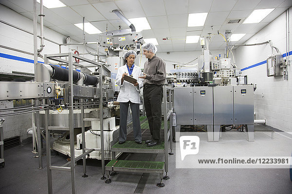 A discussion between a male Caucasian management person and a female African American technician in the bottling area of a bottled water plant.