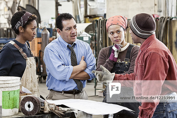 Mixed race team of workers and Hispanic man manager talking over an issue in a sheet metal factory.