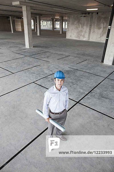 Caucasian businessman holding plans for a new office in a large empty raw office space.