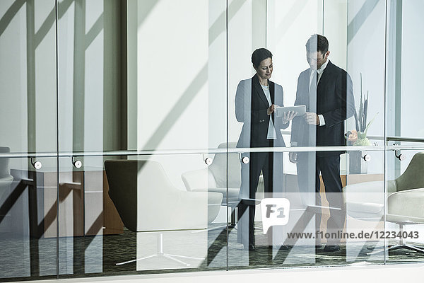 Geschäftsmann und -frau stehen hinter dem Fenster eines Konferenzraumes in einem großen Geschäftszentrum.