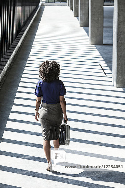 Businesswoman walking through large empty office space lit by the afternoon sun.