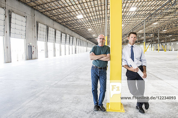 Two Caucasian men standing in front of loading dock doors in a new warehouse interior.