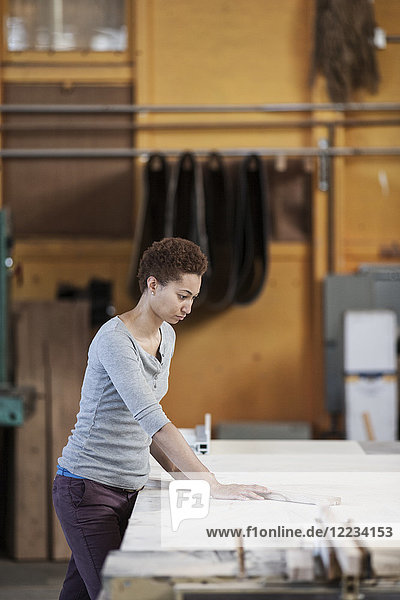 Schwarze Fabrikarbeiterin beim Vermessen von Holz an einem Arbeitsplatz in einer holzverarbeitenden Fabrik.