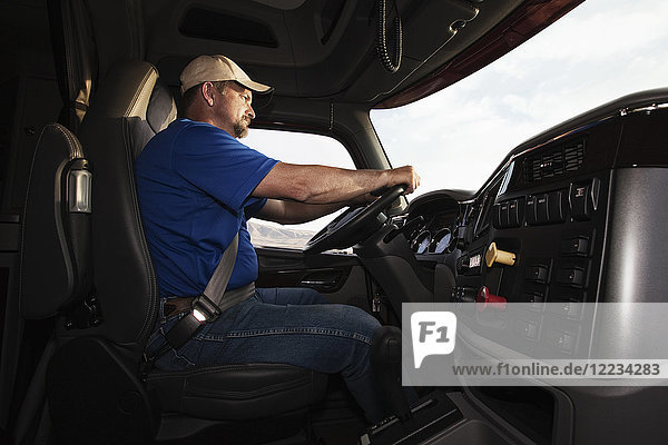 Caucasian man driver in the cab of a commercial truck.