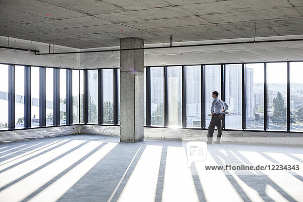 Caucasian businessman carrying plans and looking at a new empty raw office space.