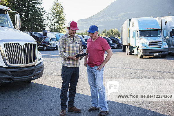 Lastwagenfahrerteam aus kaukasischen Fahrern  die auf dem Parkplatz einer Raststätte die Versandinformationen durchgehen.