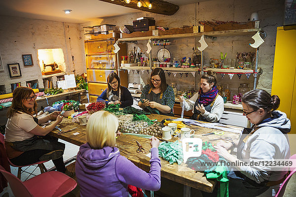 Group of people  women around a table in workshop  making paper flower wreaths.