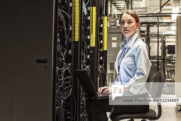 Caucasian woman technician working on computer servers in a server farm.