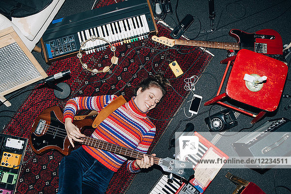 High angle view of smiling woman playing guitar while lying on carpet at studio