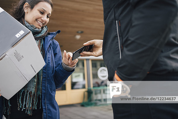 Lächelnde Frau benutzt Smartphone  um für ihre Lieferung vom Boten zu unterschreiben.