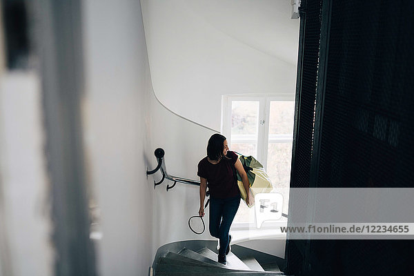 Hochwinkelansicht der Frau mit Tasche und Badmintonschläger beim Treppensteigen im neuen Haus