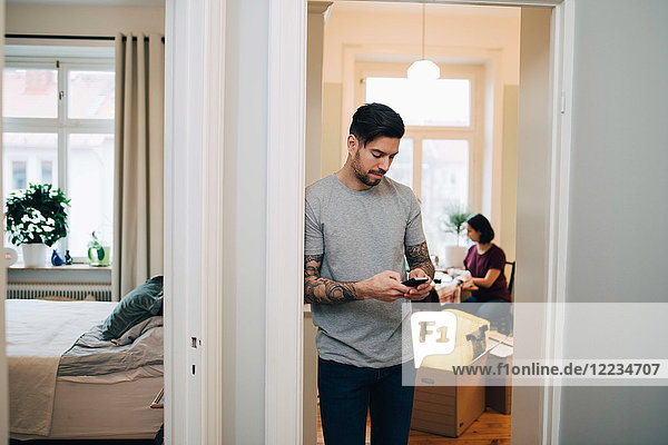 Mid adult man using mobile phone while leaning on doorway at new home
