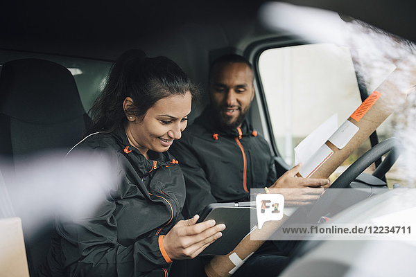 Smiling workers looking at digital tablet while sitting in delivery van