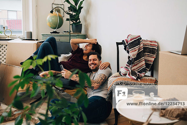 Ein glückliches Paar  das ein Smartphone benutzt  während es sich im neuen Zuhause ausruht.