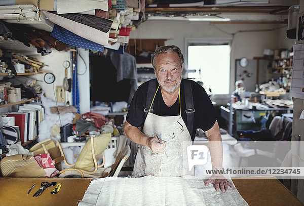 Porträt des älteren männlichen Besitzers mit Stoff an der Werkbank in der Werkstatt