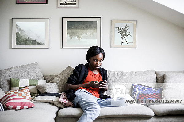 Mittlere erwachsene Frau mit Smartphone auf dem Sofa zu Hause