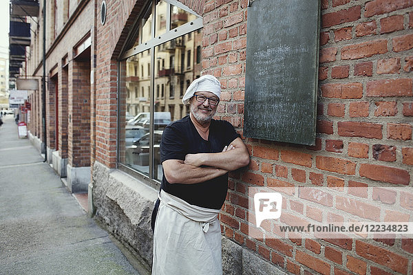 Porträt eines älteren Bäckers  der sich an die Backsteinmauer lehnt.