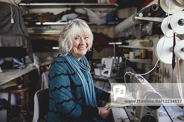 Porträt des lächelnden Seniorbesitzers an der Nähmaschine in der Werkstatt