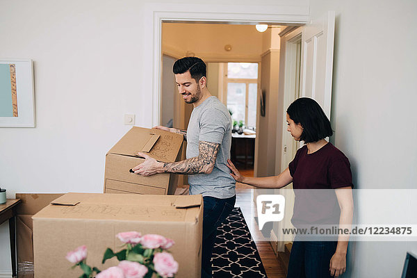Woman standing by man carrying cardboard box in living room