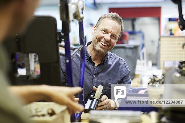 Lächelnder  reifer Freiwilliger  der den männlichen Kollegen in der Werkstatt ansieht.