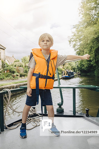 Volle Länge des selbstbewussten Jungen  der das Boot im Fluss gegen den Himmel steuert.
