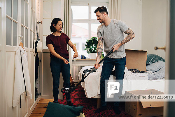 Woman gesturing while man holding golf club by bed in bedroom during relocation