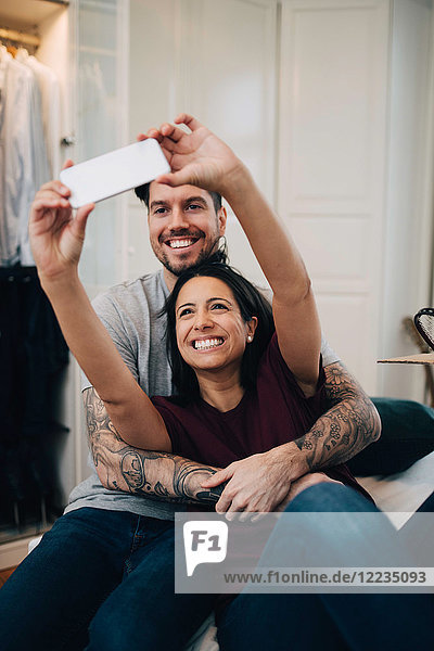 Lächelndes Paar nimmt Selfie auf dem Handy  während es sich im Schlafzimmer auf dem Bett ausruht.