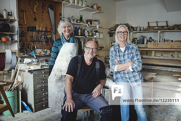 Porträt von lächelnden Seniorinnen und Seniorinnen  die in der Werkstatt gegen Werkzeuge stehen