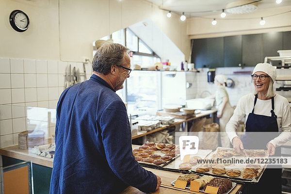 Lächelnde Besitzerin zeigt dem Kunden in der Bäckerei frische Backwaren.